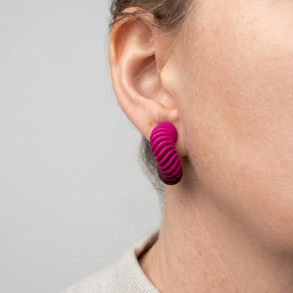 A pink gradient 3d printed twisted hoop earrings on a an woman's ear by Phase Jewellery